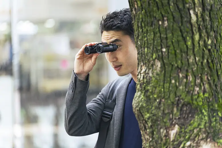 写真：木に隠れて双眼鏡を持って見張りをする男性